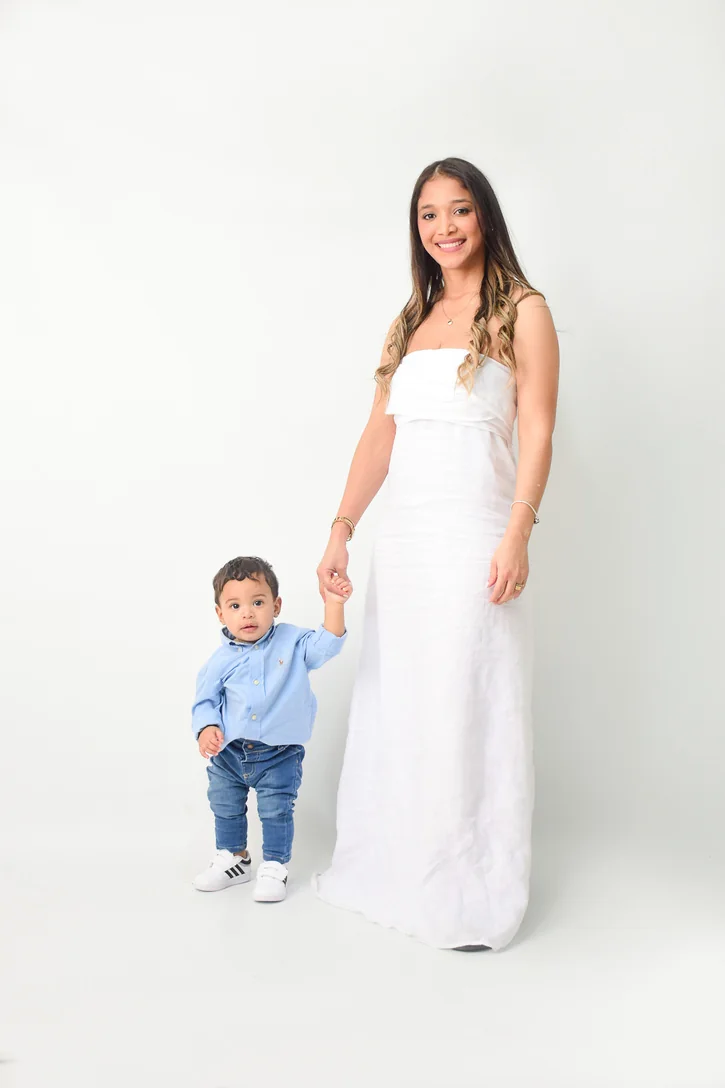 Mamá de vestido largo blanco de la mano de su bebé en estudio